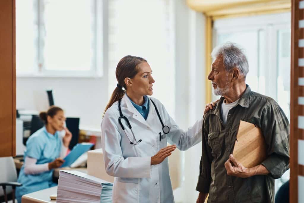 Female doctor communicating with senior man in hallway at medical clinic.
