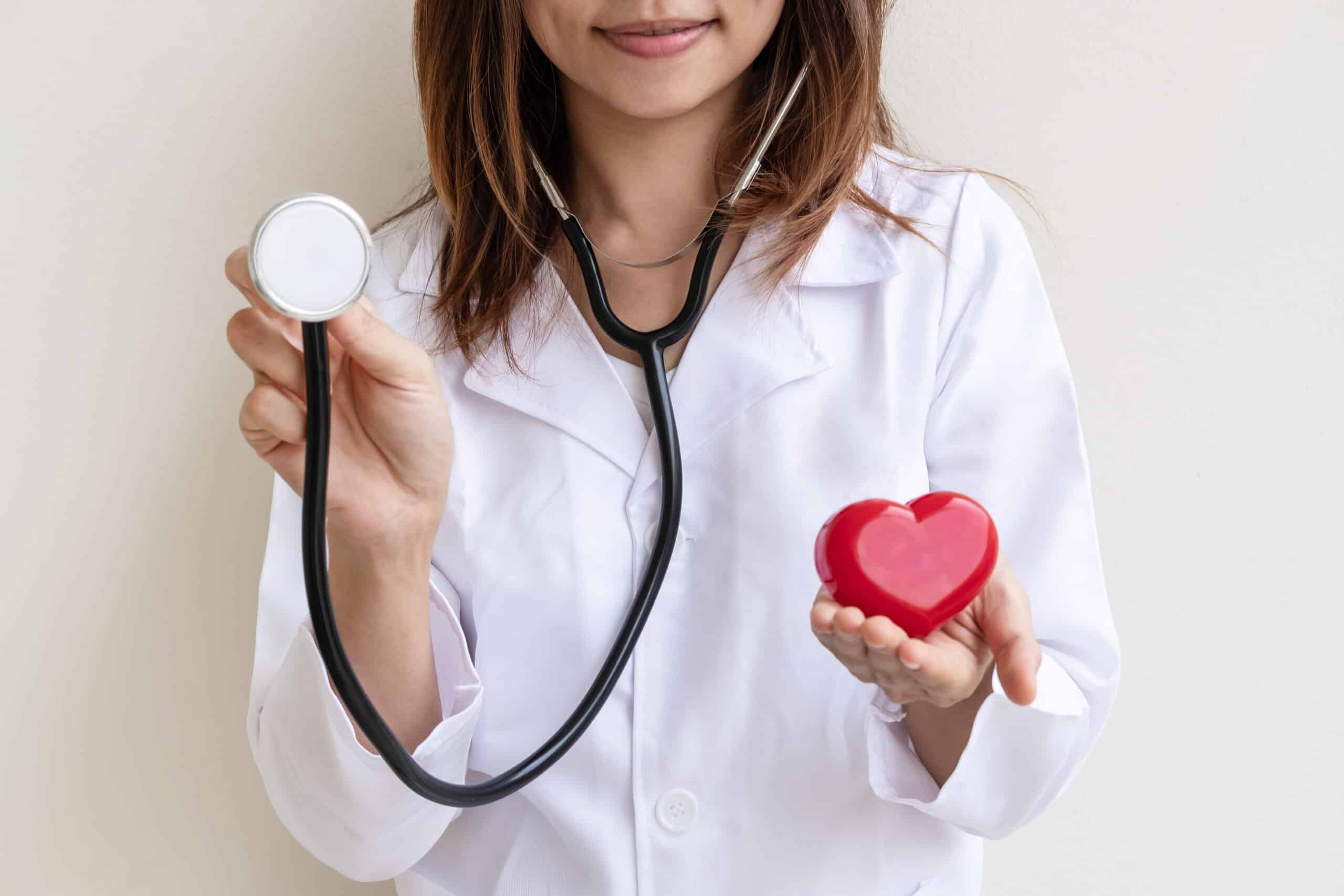 Young female doctor with the stethoscope holding red heart, cardiolog healthy care concept